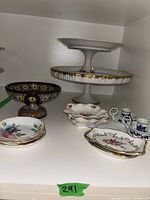 White two-tiered ceramic pedestal serving tray, floral-shaped serving trays, blue and white ceramic double candle holder, small decorative plates, and large multi-colored pedestal serving bowl.