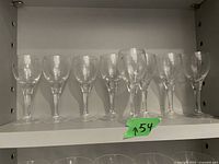 22 clear glass sherry glasses lined up on a shelf with a small green marker showing number 154