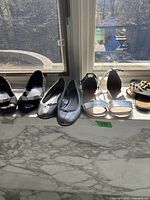 Photo of five pairs of women's shoes placed on a windowsill in sunlight showing different styles including flats and sandals.