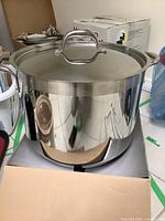 Large stainless steel stockpot with lid sitting in an open box.