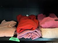 Three folded cashmere sweaters on a dark shelf, peach, red, purple shades