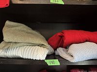 Two folded sweaters on a dark shelf, one red and one light grey knit with textured pattern.