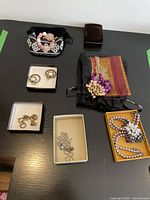 Full overview of all jewelry pieces including earrings, necklaces, bracelet, and pouches on black surface.