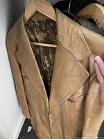 Tan leather jacket hanging on wooden hanger showing front, lapel collar, zip pockets and printed lining