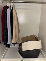 Five women's coats and blazers hanging on hangers in a closet, colors red, navy striped, light blue, black, beige.