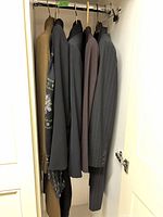 Five jackets and suits hanging in closet, showing variety and colors.