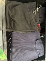 Black crew neck and navy blue ribbed knit turtleneck sweaters folded side by side in drawer