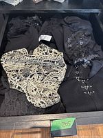 Drawer of black women's blouses including one with gold lace overlay and others with varying textures.