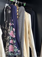 Five garments hanging on a rack showing floral chiffon blouse, navy embroidered top, striped blazer, ivory jacket and black piece