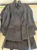Gray women's coat laid flat showing front with high collar and side slit details trimmed with black leather or faux leather.