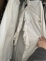 White dress shirt with ruffle front detail seen hanging in closet.