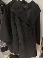 Textured black women's coat by BCBG hanging with other coats, showing large lapel collar and single button detail.