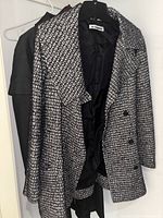Two coats hanging side by side on hangers: black and white patterned coat in front, grey trench coat behind