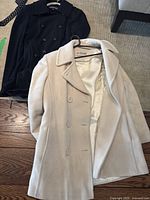 Photo showing two women's coats, one beige on a hanger and one black on floor, placed side-by-side.