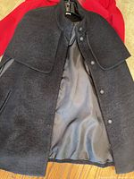 Black women's coat with button closure and cape detail, open showing smooth lining.