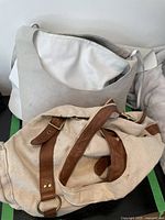 Two shoulder bags, one white and beige fabric bag and one beige canvas bag with brown leather straps and brass hardware.