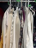 View of clothing rack with multiple women's vintage clothing items in cream, white, beige, and floral prints hung on hangers.