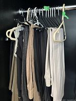 Photo showing multiple pairs of women's trousers hanging on a rod including various colors such as black, beige, grey.
