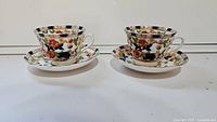 Pair of Burham porcelain teacups with matching saucers, decorated with floral and navy blue patterns, shown from the front on a white background.
