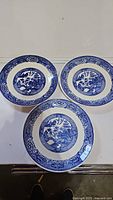 Three vintage round plates with blue and white Blue Willow style designs laid out on a white surface.