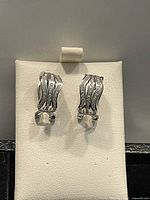 Front view of sterling silver loop earrings with wave pattern and embedded Swarovski crystals on white jewelry display.