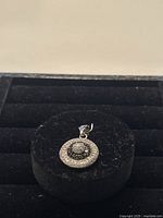 Small round pendant with concentric circles of black and clear Swarovski crystals on a silver base displayed on black velvet.