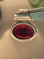 Close-up photo showing the silver bail engraved with 925 and PRM hallmark and the deep red faceted crystal