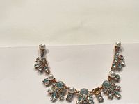 Front view of gold-tone statement necklace with large clear rhinestones and faux pearls laid flat on white background.