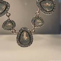 Close-up image showing pear-shaped moonstone-colored Swarovski crystal surrounded by small clear rhinestones on silver-tone setting.
