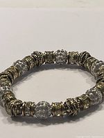 Close-up image of an elastic bracelet featuring clear crystal beads with raised dots and ornate gold plated metal charm beads with textured detailing, arranged in alternating pattern.