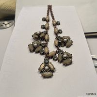 Full view of the necklace laid out on a flat white surface showing the design of pendant clusters along the chain.