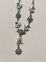 Full view of the silver-tone chain necklace with flower-shaped rhinestones and crystal centers accented with milky leaf-shaped decorations.