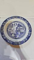 Top-down view of a vintage Blue Willow pattern plate featuring traditional scenic design in blue and white.