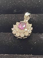 Close-up photo of Swarovski pendant showing pink center crystal surrounded by clear stones in silver-tone setting on black background.