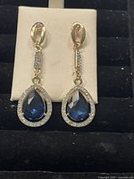 Front view of the Swarovski crystal earrings showing blue teardrop center and clear crystal halo on gold-tone setting.