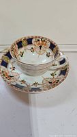 Side view of the teacup on the saucer showing detailed floral and gold pattern with dark blue border.