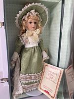 Porcelain doll in green lace dress inside suitcase with authenticity papers visible