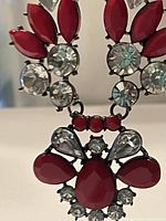 Close up image of the necklace pendant featuring clear rhinestones and red marquise and teardrop shaped stones arranged in a star pattern.