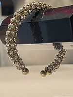 Close-up side view of the rhinestone encrusted open bangle showing the gold-tone ball ends.