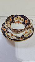 View of teacup and saucer set showing ornate blue and gold floral pattern with scalloped edges.