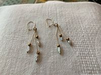 Photo showing both 10K gold earrings with three dangling strands and freshwater pearl ends, laid flat on a textured light fabric surface.