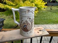 Full side view of white pottery pitcher showing gold floral designs and portrait of Queen Victoria.