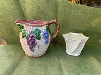Photo of both items on green fabric showing the jug with grape decoration and Belleek planter.