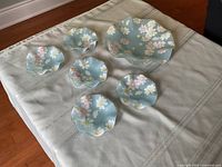 Full set of one large and five small blue glass serving dishes arranged on a table, showing the scalloped edges and flower designs.