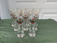 Front view of 9 Carlsberg Red beer glasses arranged on a green cloth, showing logos and gold rims