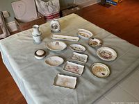Top view of vintage Limoges trinket dishes in various shapes including oval, round, rectangular with floral decoration, vases, small clock, and trinket box placed on a cloth-covered table.
