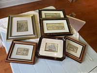 Overview of six framed embossed silver pictures with different scenery and frame styles placed on a table.