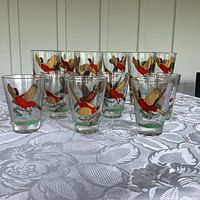 Set of 12 Hazel Atlas vintage bar glasses with pheasant design and gold trim arranged on table.