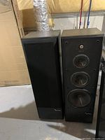 Pair of speakers side by side, one grille off showing drivers