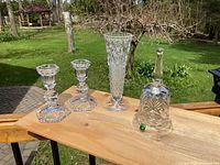 Wide shot of the crystal bell, candlesticks, and vase arranged on a wooden surface outdoors.